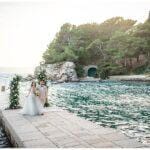 Brautpaar auf Stein Steg im Meer mit Traubogen aus blättern und weißen Rosen