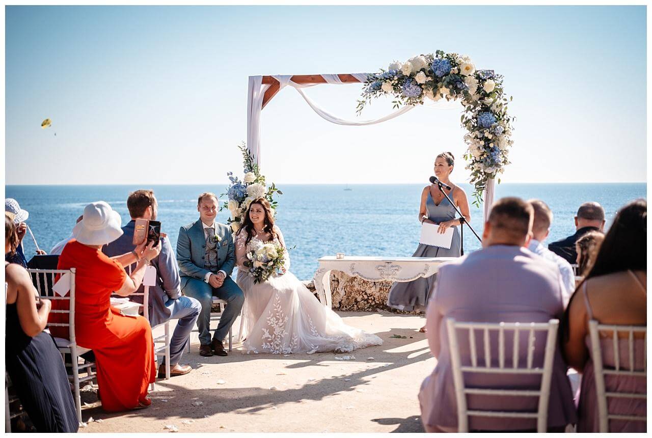 Freie Trauung mit dem Blick aufs Meer und Traubogen aus Holz mit weißen Stoff und blau weißen Blumen bei einer Hochzeit in einer privaten Finka in Kroatien