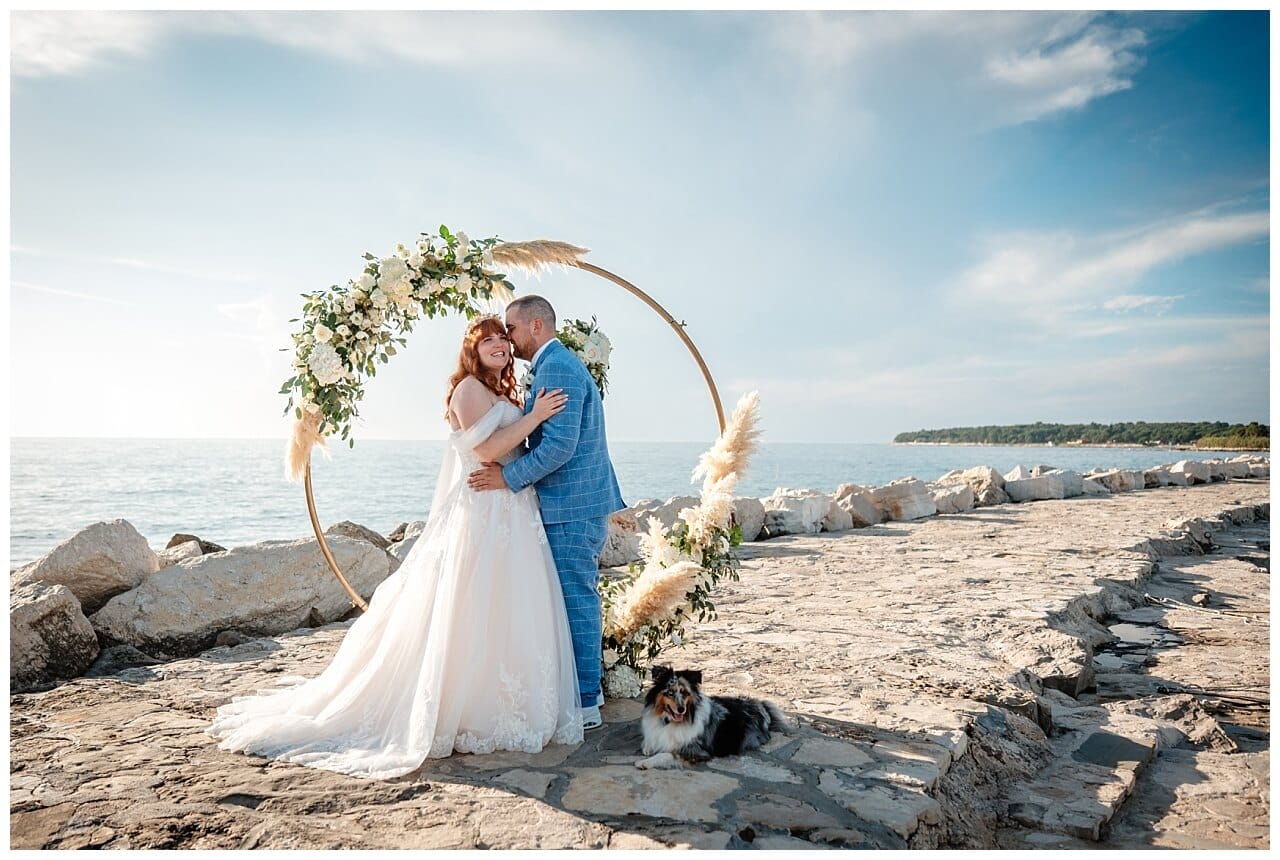 Brautpaar vor Holz Traubogen mit boho Blume Dekoration in weiß am Meer