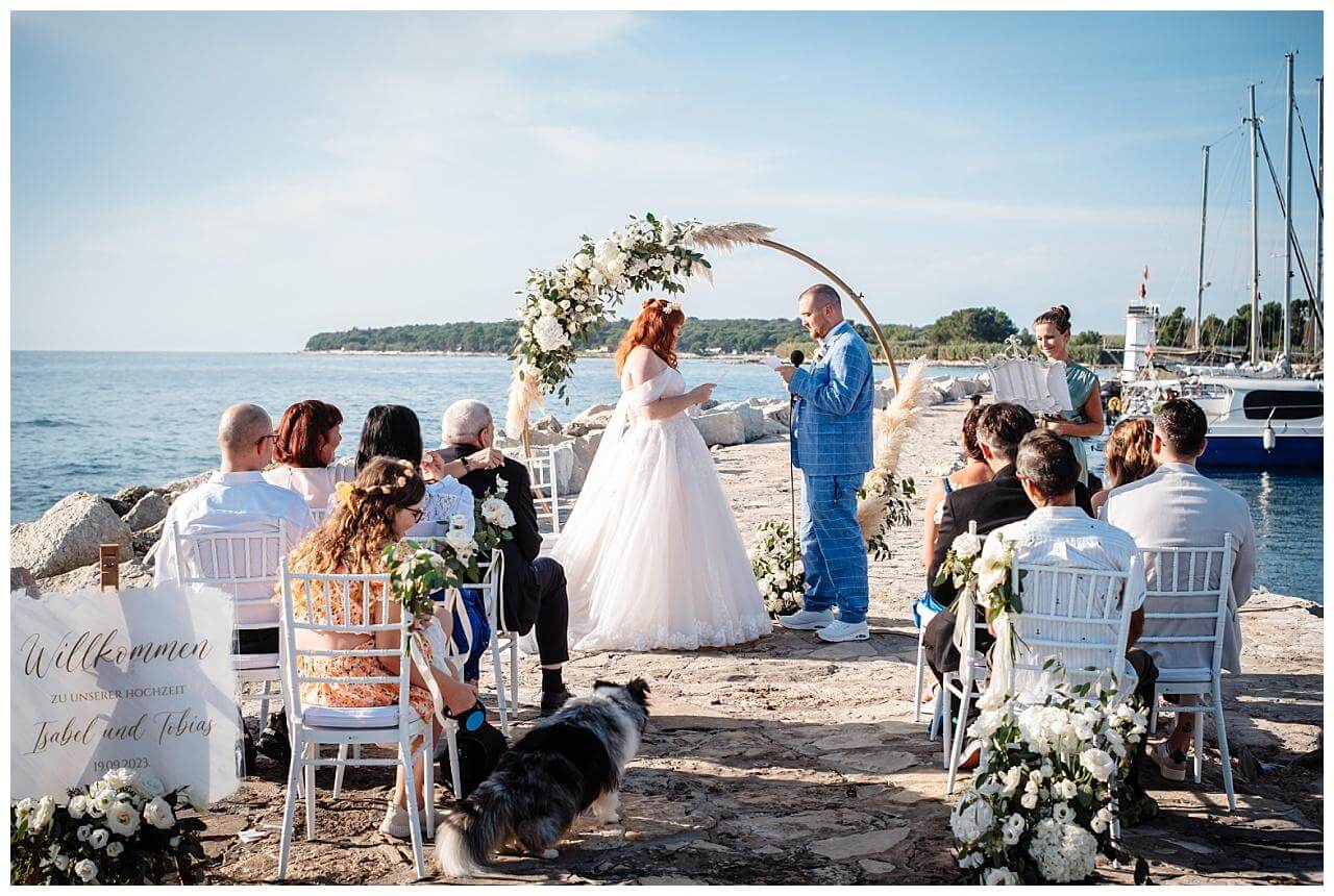 Brautpaar vor Holz Traubogen bei ihrer Trauung mit boho Blume Dekoration in weiß am Meer in Kroatien